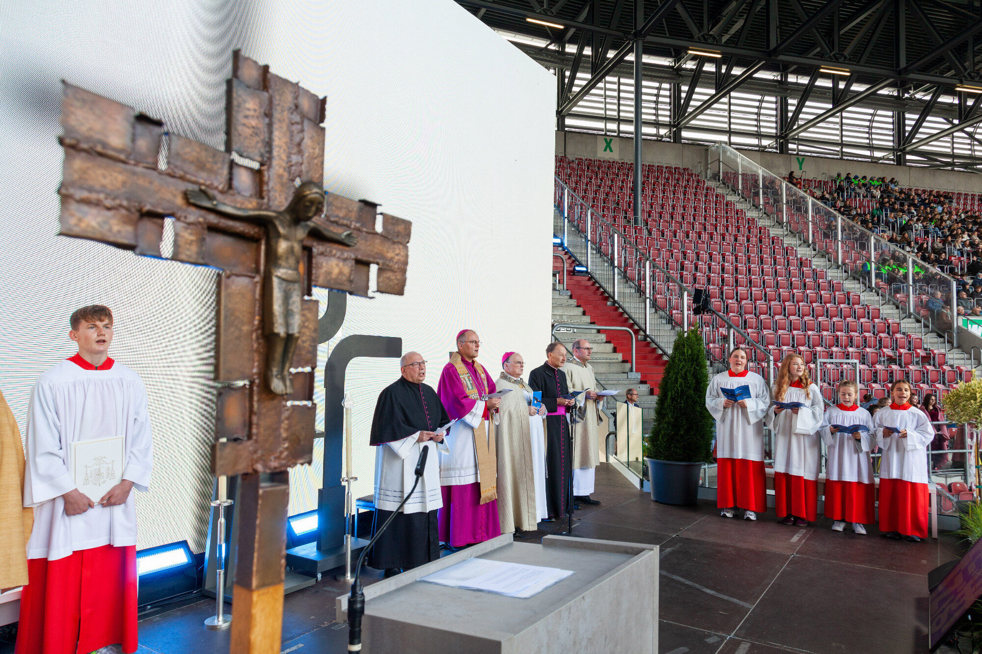 Kruzifix, Ministrant und Geistliche vor den Rängen, WWK Arena Augsburg / Schulwerk