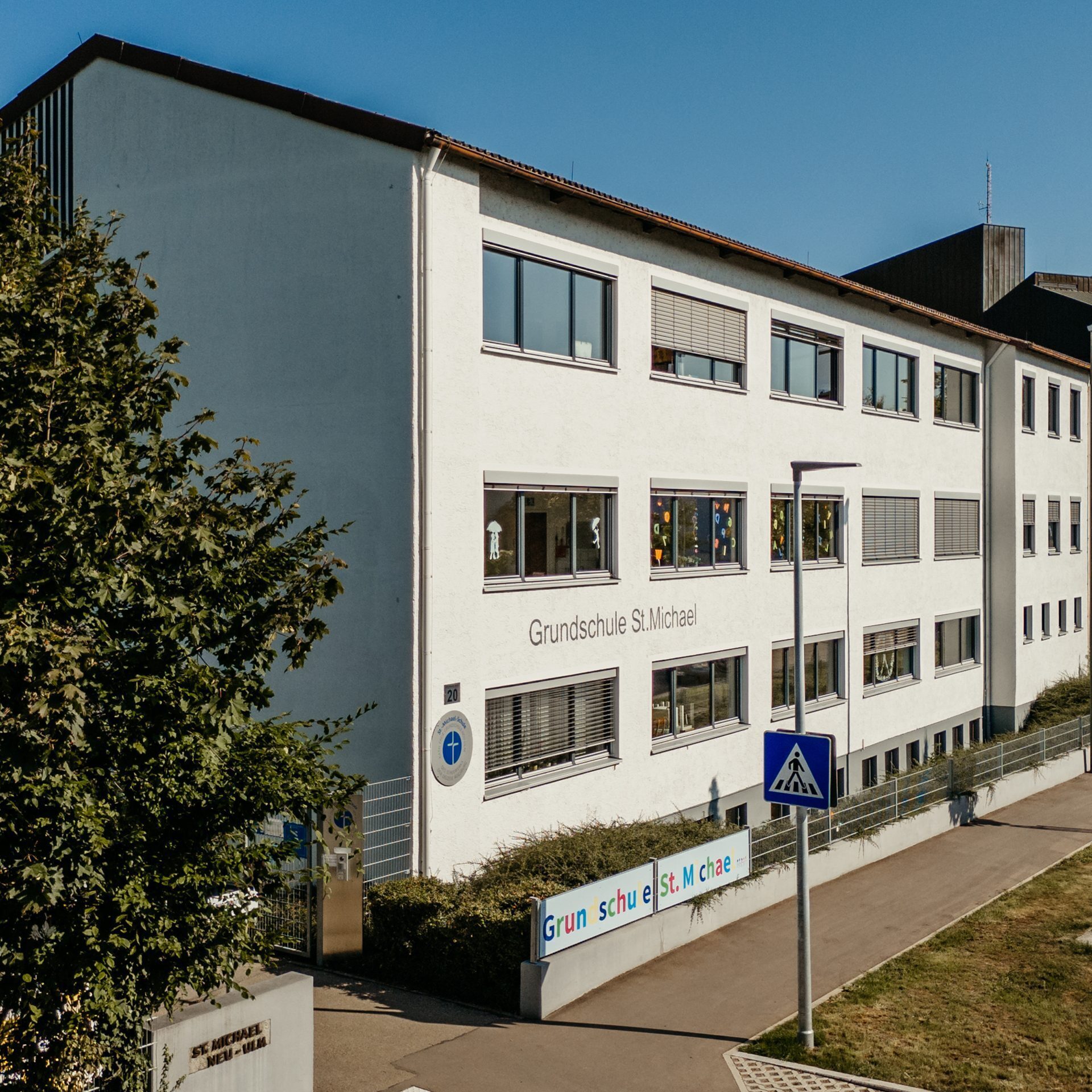 Weißes Schulgebäude der Grundschule St. Michael in Neu-Ulm mit buntem Schriftzug an der Straße