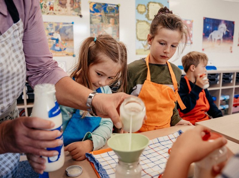 Kinder in der Koch-AG füllen Milch durch einen Trichter, St.-Michael-Grundschule Neu-Ulm